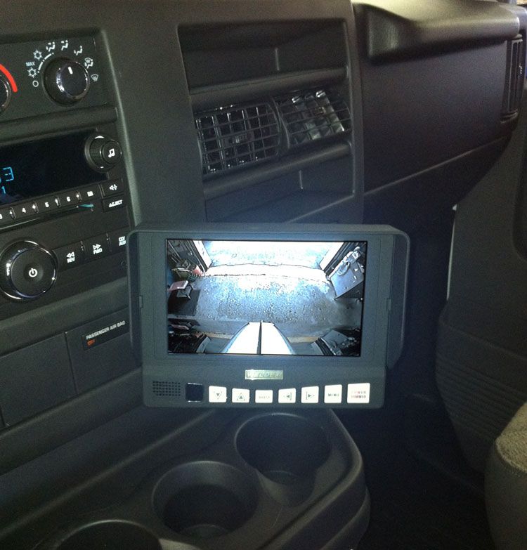 Dashboard with rearview camera monitor showing the back of a vehicle; dark interior.