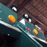 Green truck detail with orange and white lights, against a brown, industrial background.