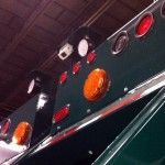 Green semi-truck cab with red and amber lights against a dark ceiling.