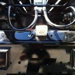 Close-up of a black vehicle's undercarriage with curved metal pipes, a light, and a reflective surface.