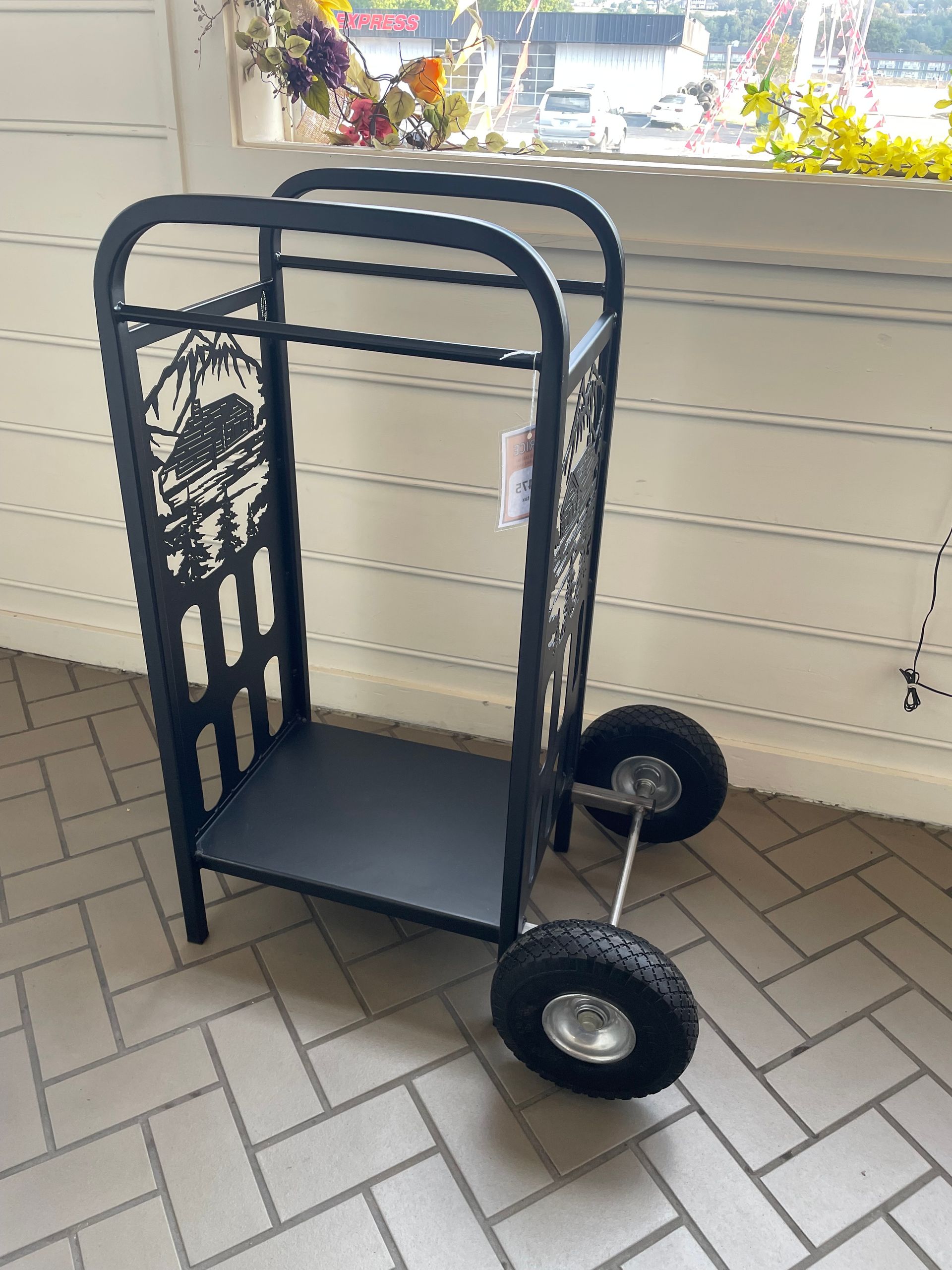 A black cart with wheels is sitting on a brick floor in front of a window.