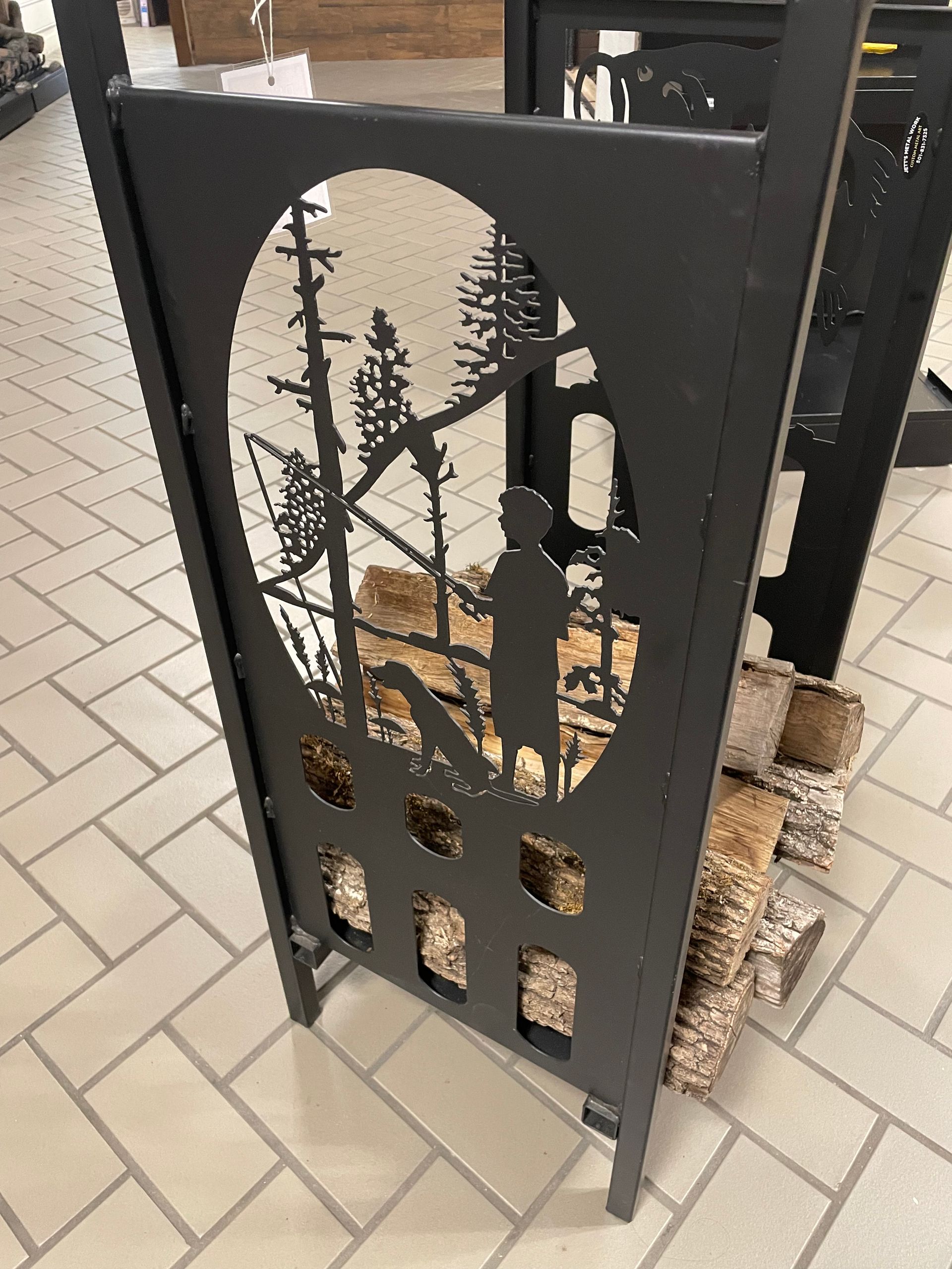 A black metal firewood rack with a silhouette of a man and trees on it.