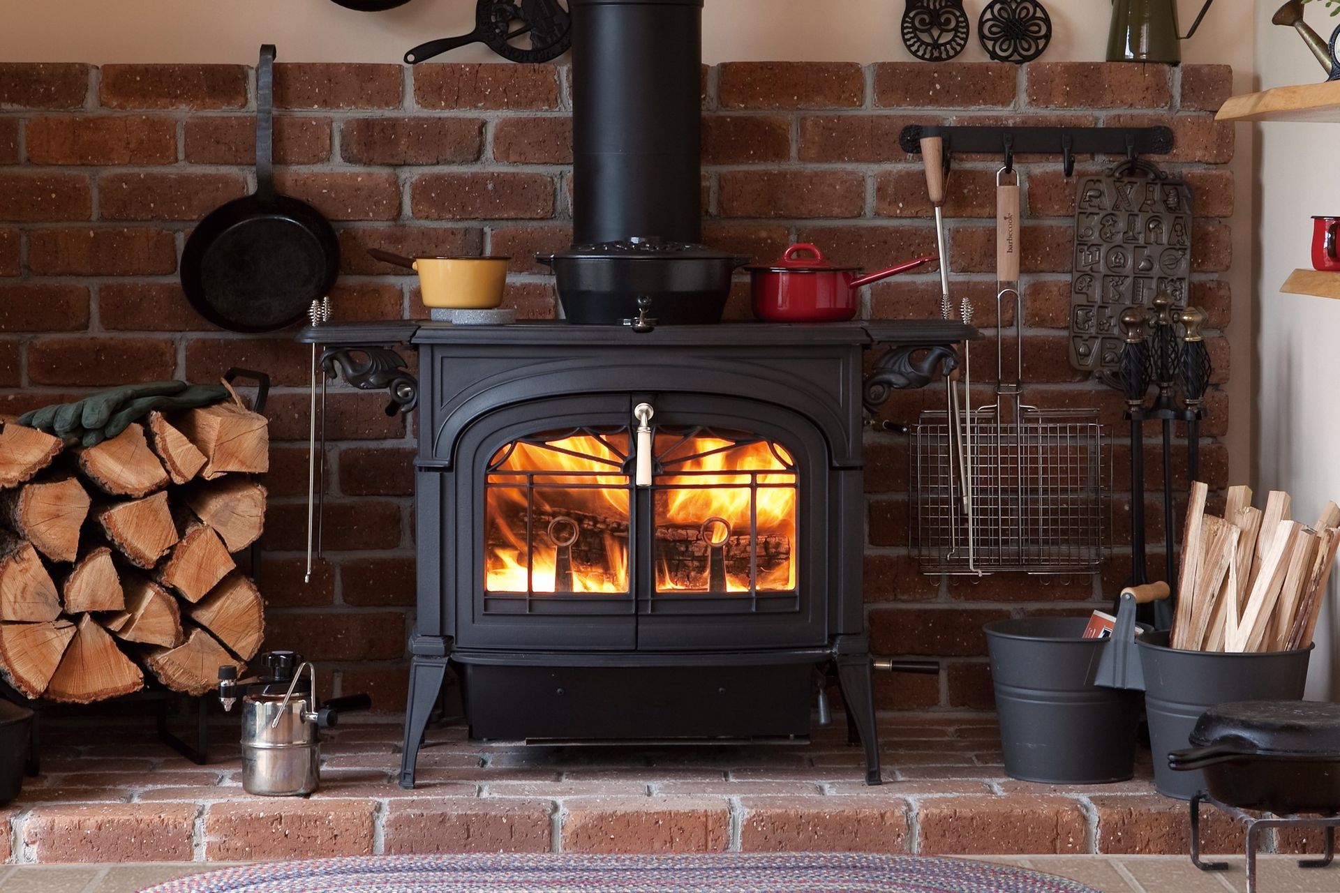 A wood stove is sitting in front of a brick wall.