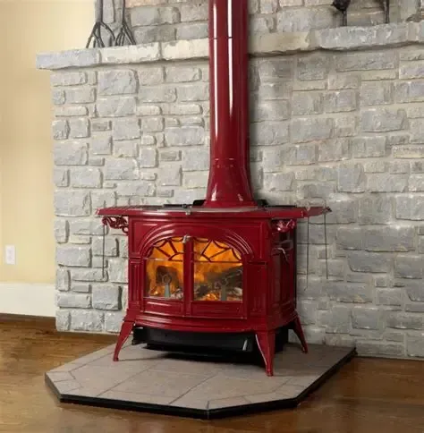 A red wood stove is sitting in a stone fireplace.
