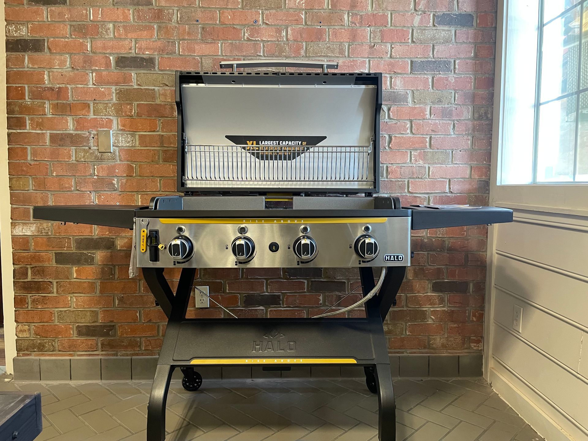 A gas grill is sitting in front of a brick wall.