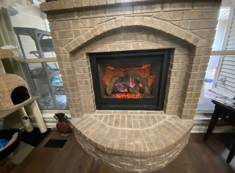 There is a fireplace in the middle of the room with a cat tree in the background.