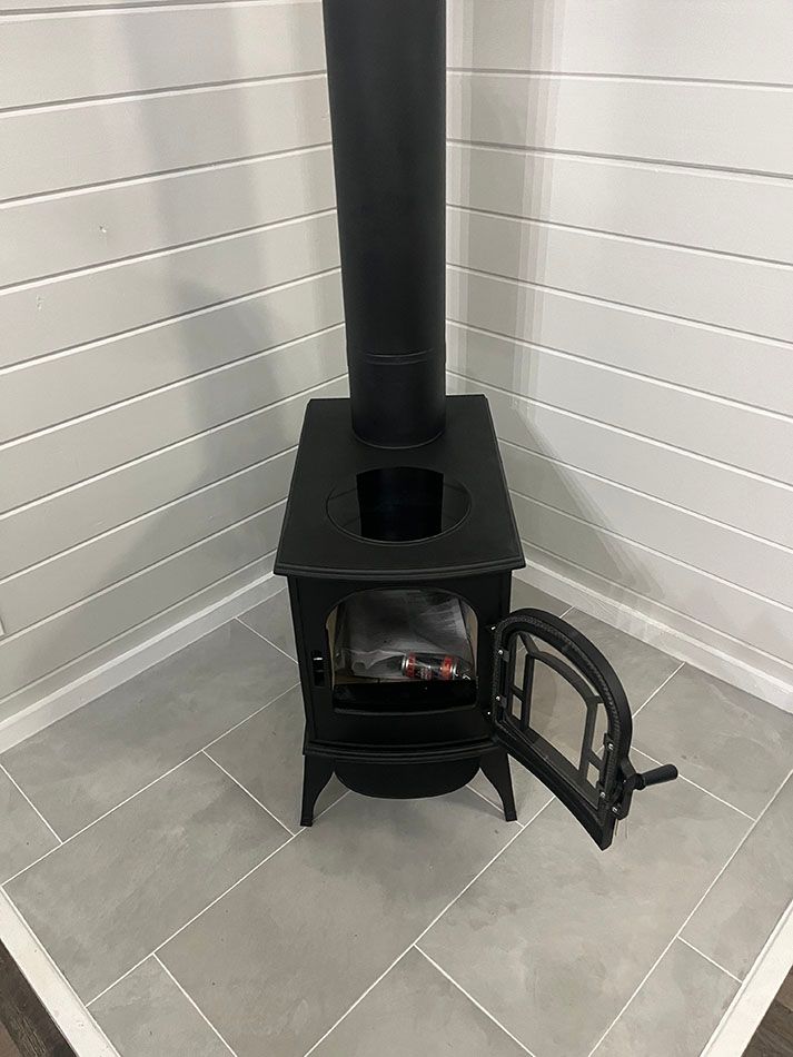 A wood stove is sitting in a corner of a room with its door open.