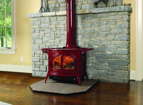A red wood stove is sitting in front of a stone fireplace.