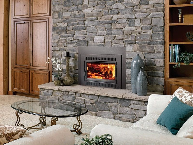 Stone fireplace with lit fire in a cozy living room, flanked by wood cabinets and glass decor