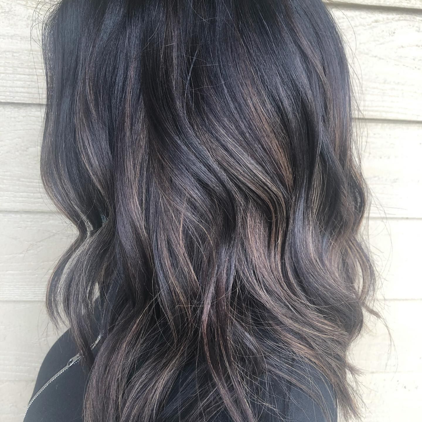 A woman with long dark hair is standing in front of a wooden wall.