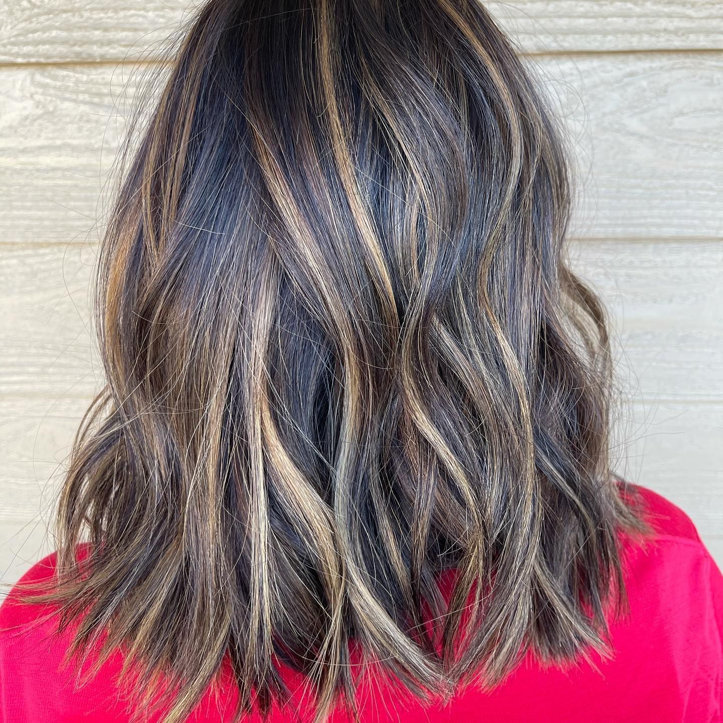 The back of a woman 's hair with highlights and a red shirt.