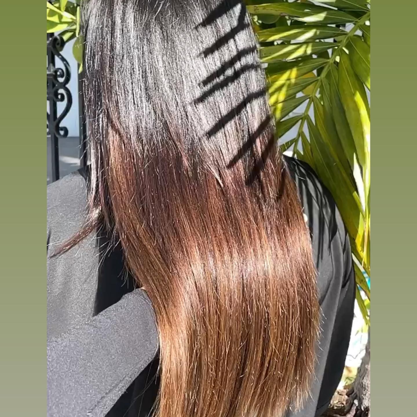 A woman with long hair is standing in front of a palm tree.