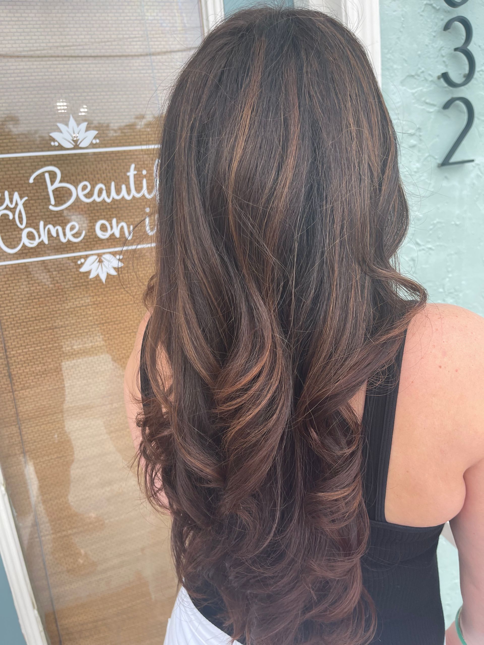 A woman with long brown hair is standing in front of a window.
