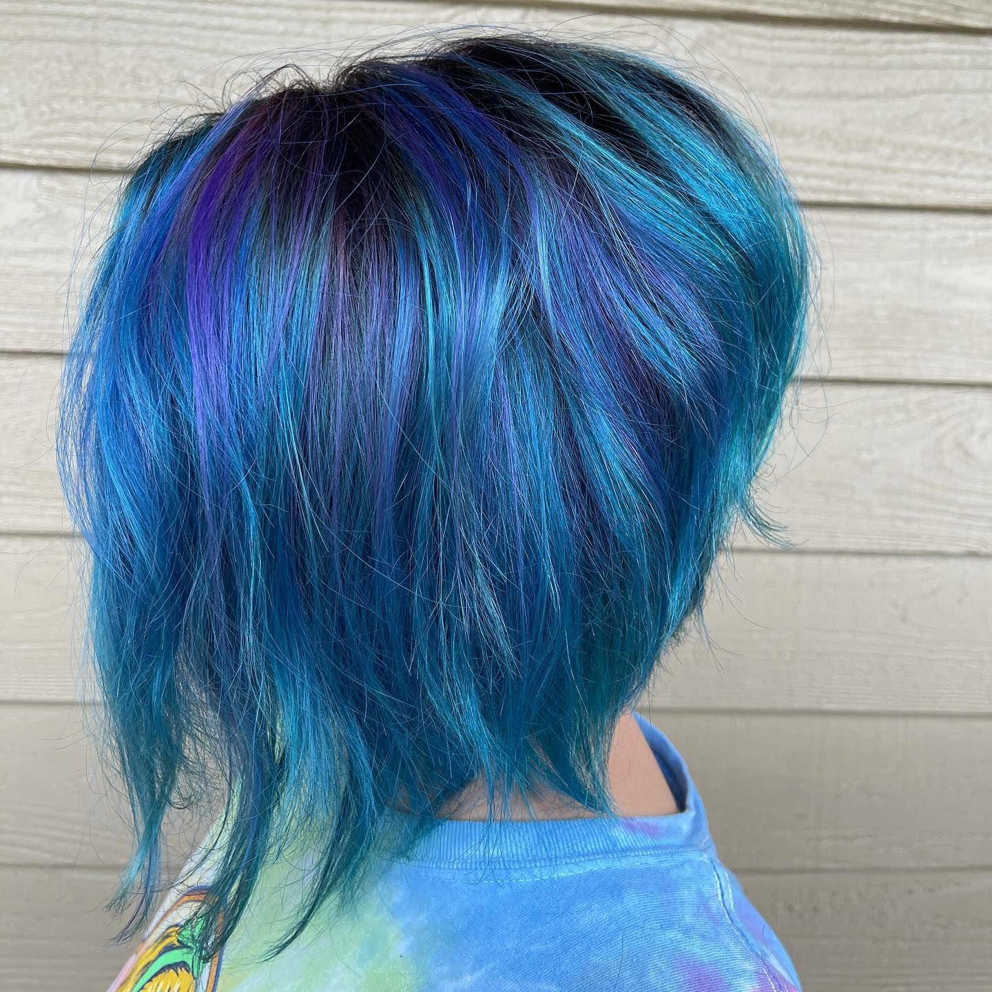 A woman with blue and purple hair is wearing a tie dye shirt.