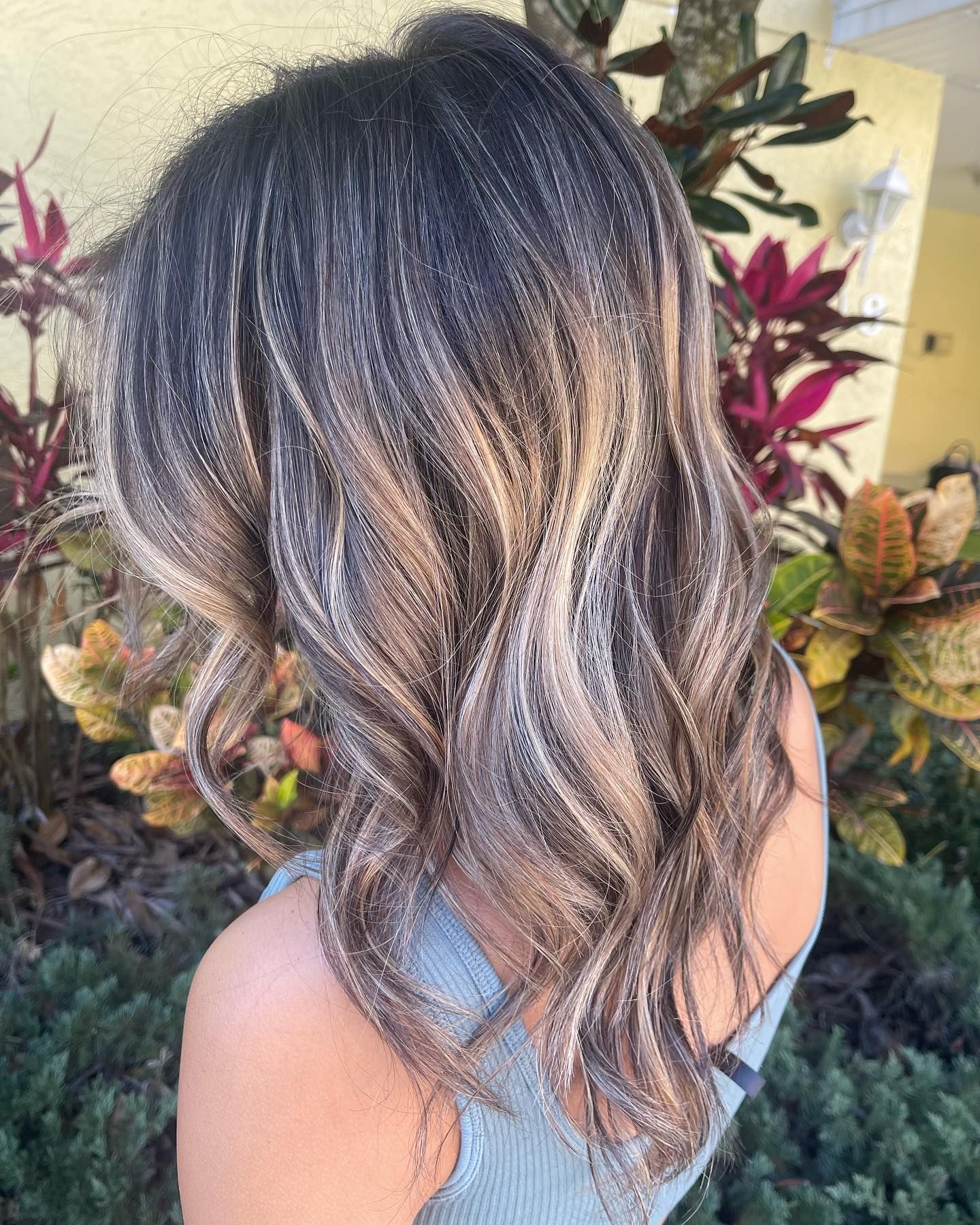 A woman with long hair is standing in front of a bush.
