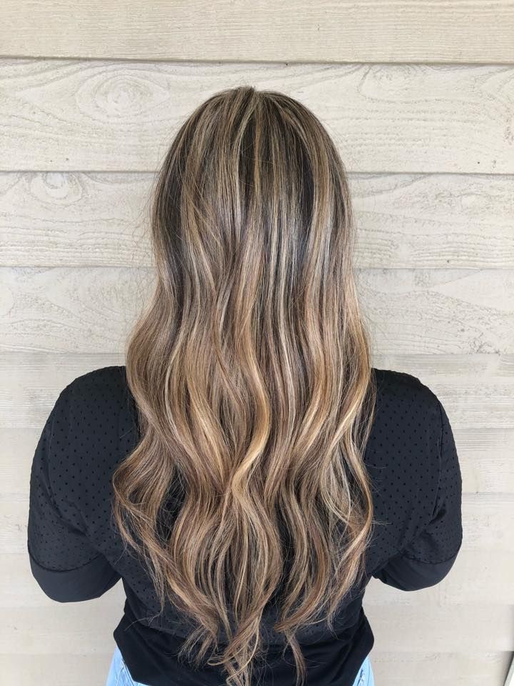 A woman with long brown hair is standing in front of a wooden wall.
