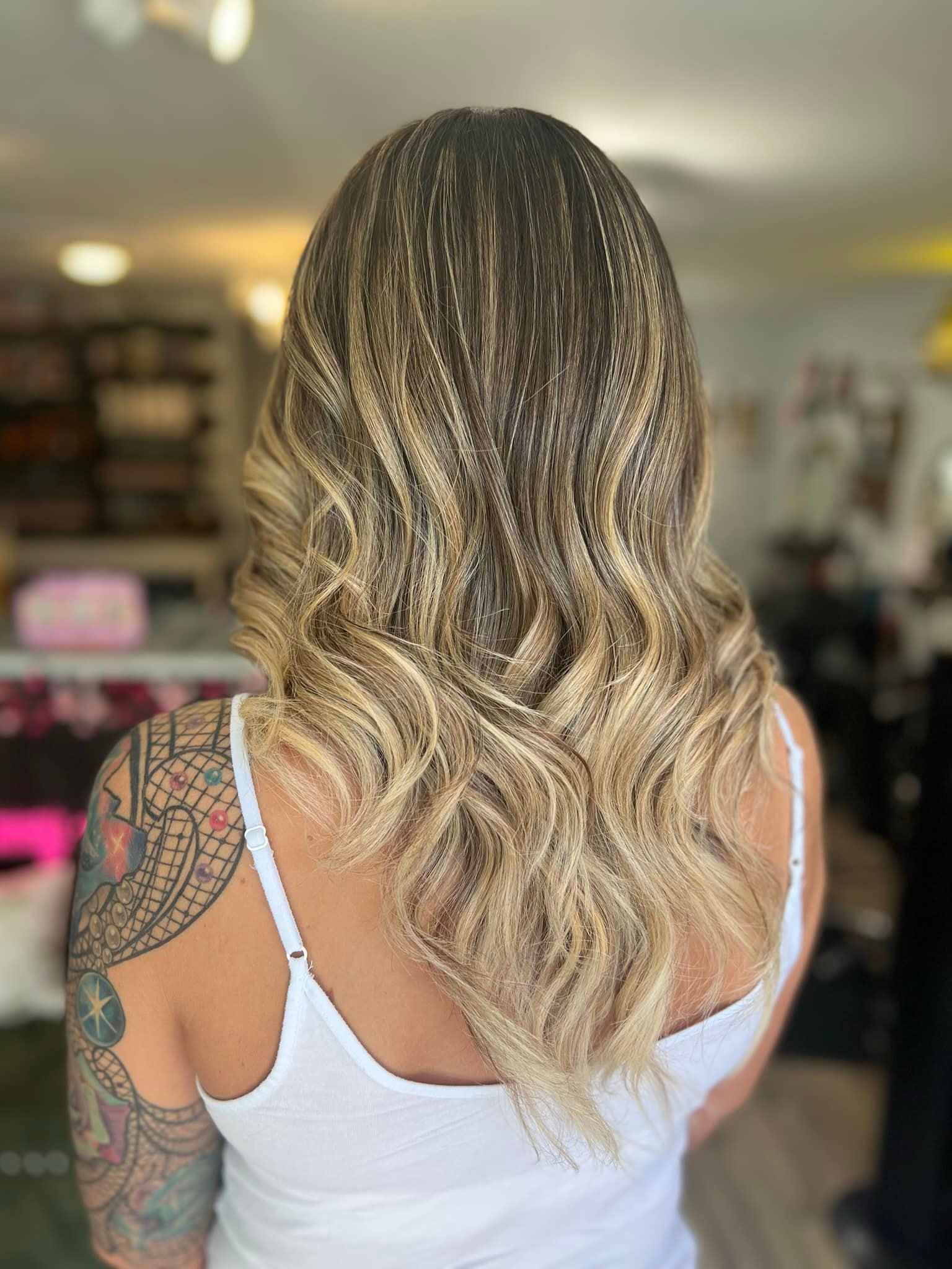 The back of a woman with long blonde hair and a tattoo on her arm.