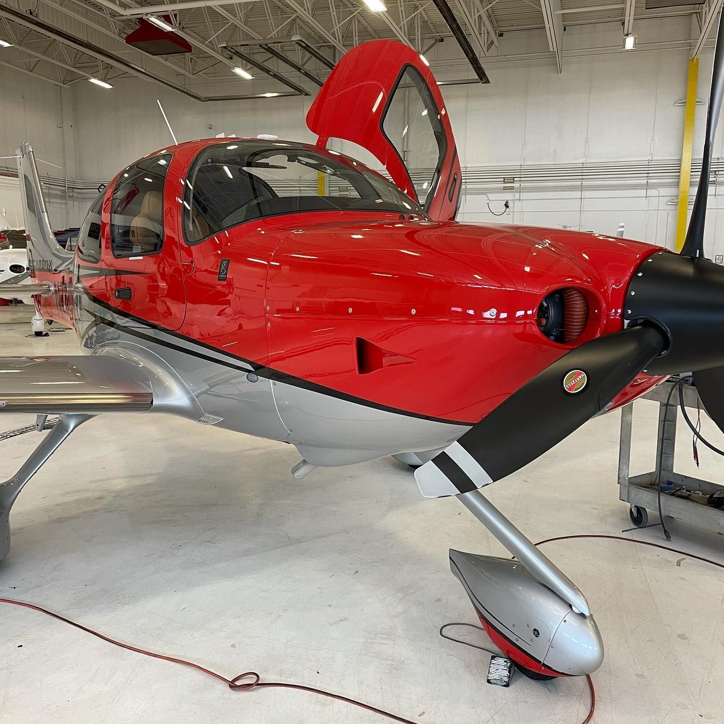 Red single-engine airplane in a hangar with its canopy open, showing a glossy red and gray body.