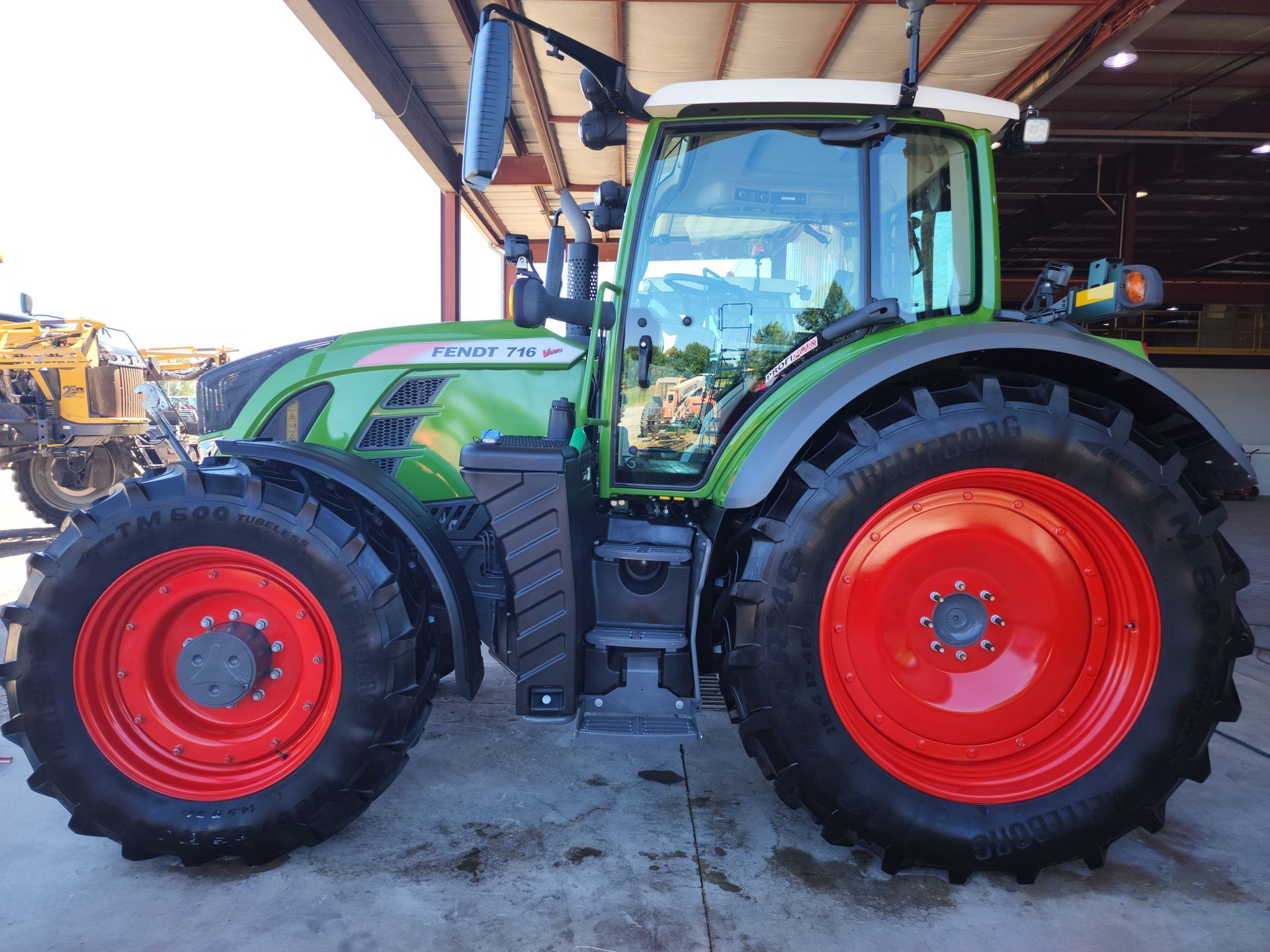 Green tractor with red wheels parked under a shed