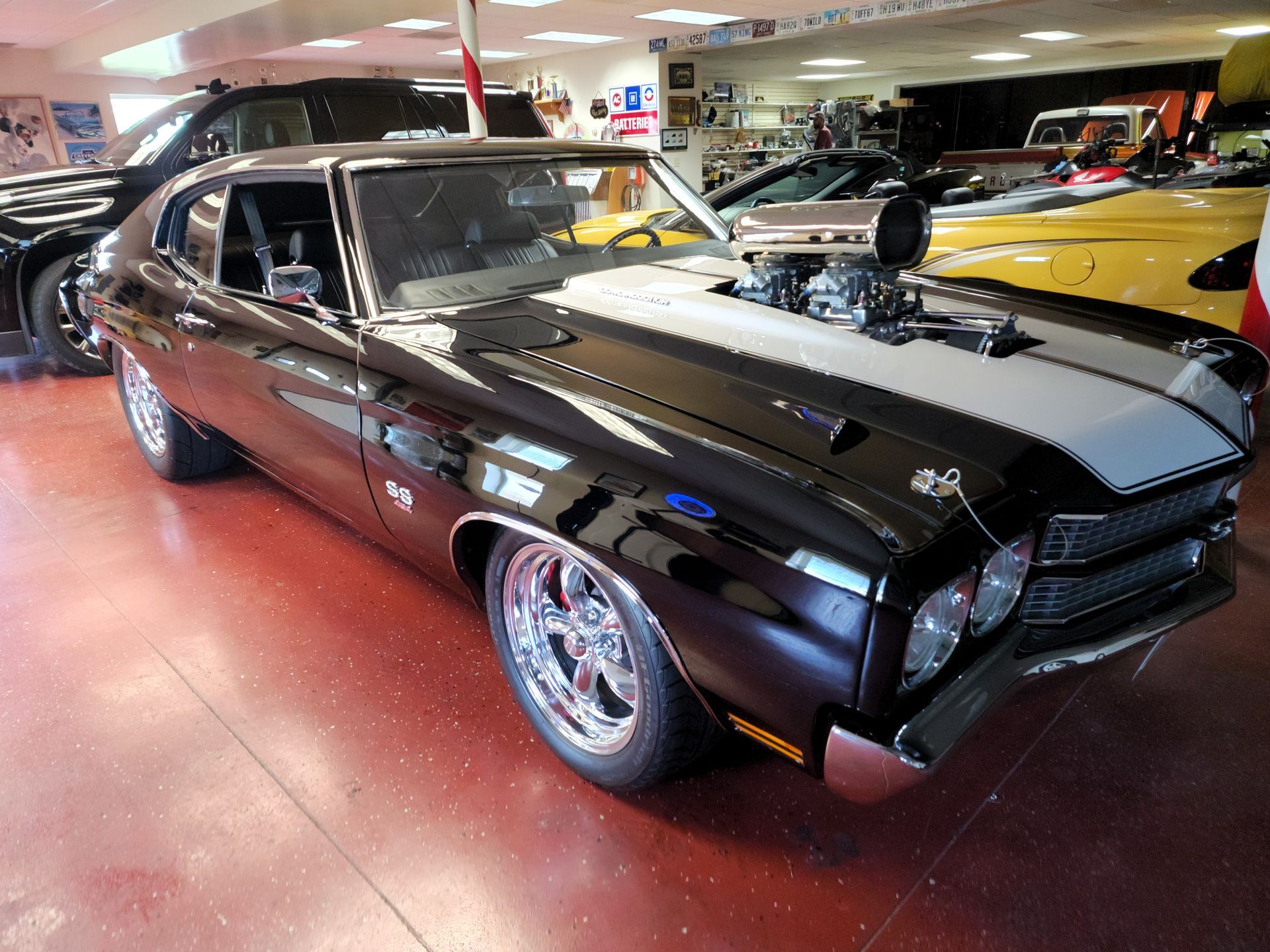 Black classic muscle car with hood scoop displayed indoors under showroom lights