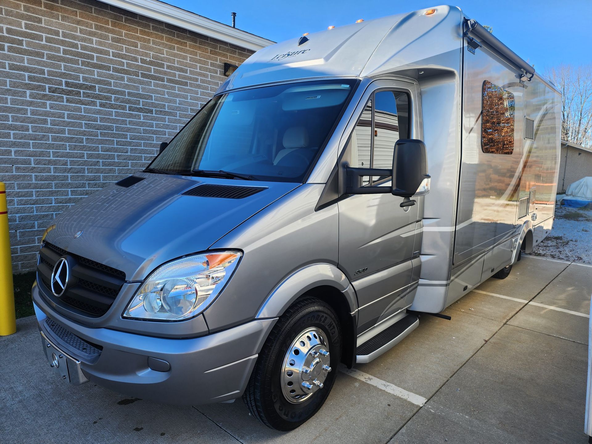 Silver Mercedes Sprinter van parked beside a brick building on a sunny day