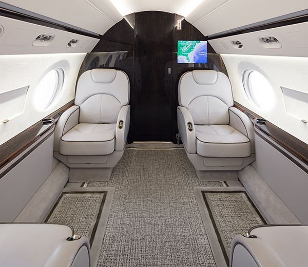 Luxury private jet cabin with two white leather seats and a small monitor in front, in a sleek gray interior