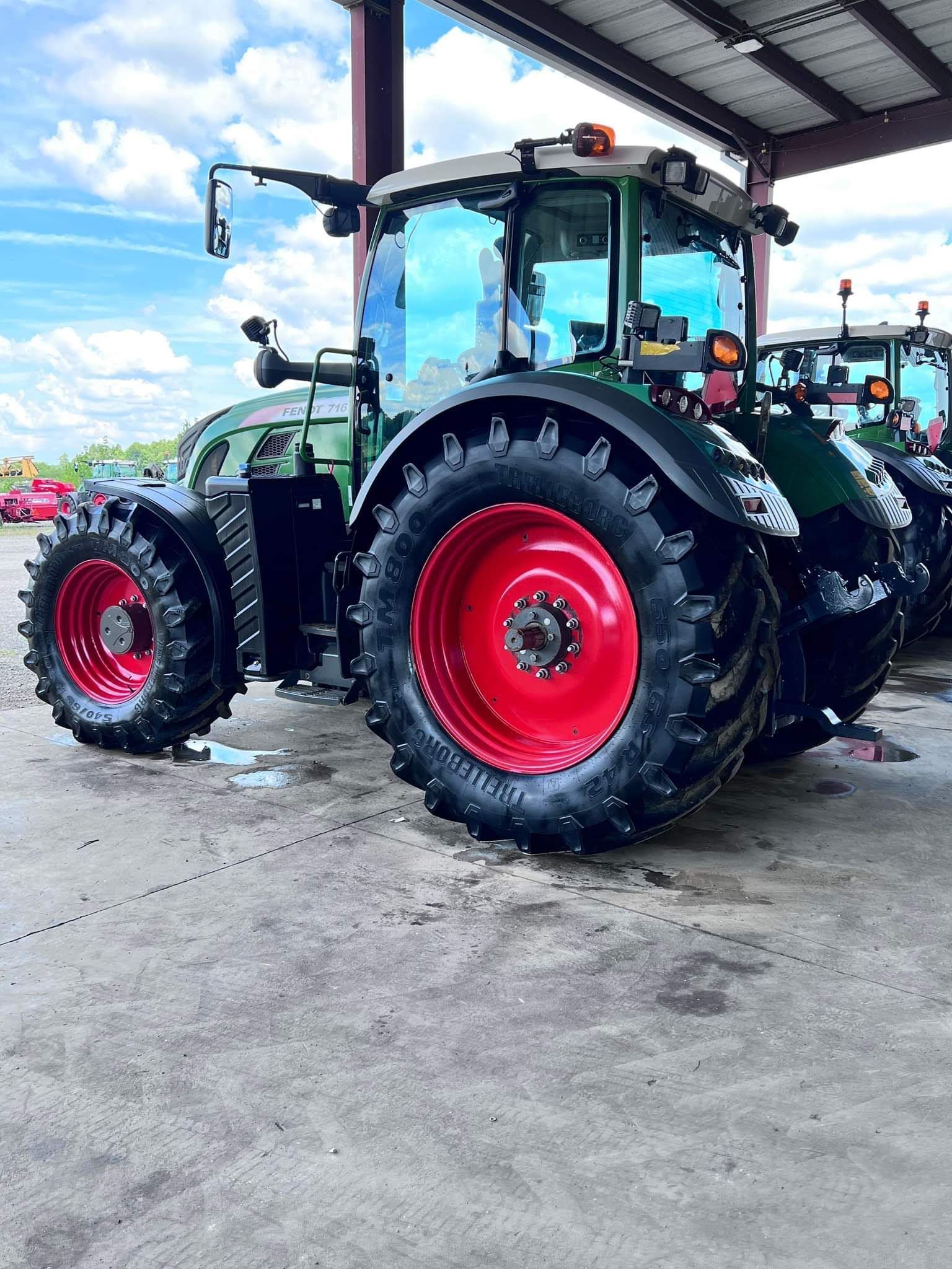Two black tractors with bright red wheels parked under a metal shed on a concrete lot.
