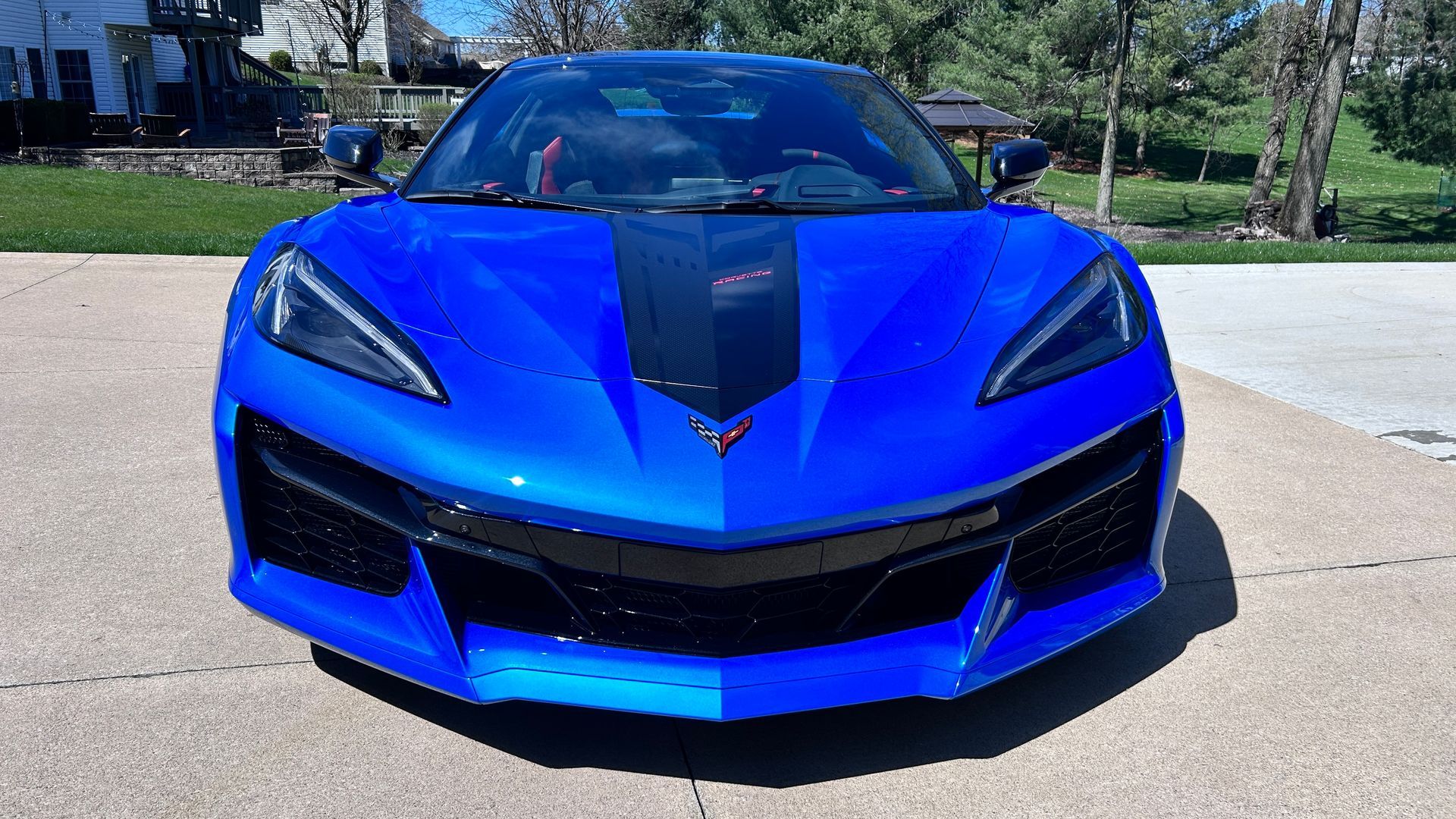 Front view of a bright blue sports car with black accents parked outdoors in sunlight
