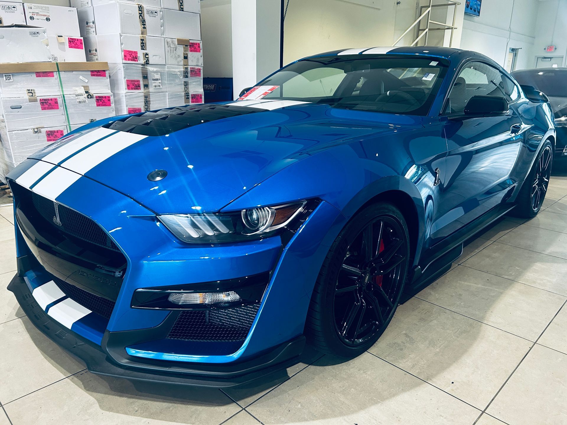 Blue sports car with white racing stripes parked indoors on a showroom floor