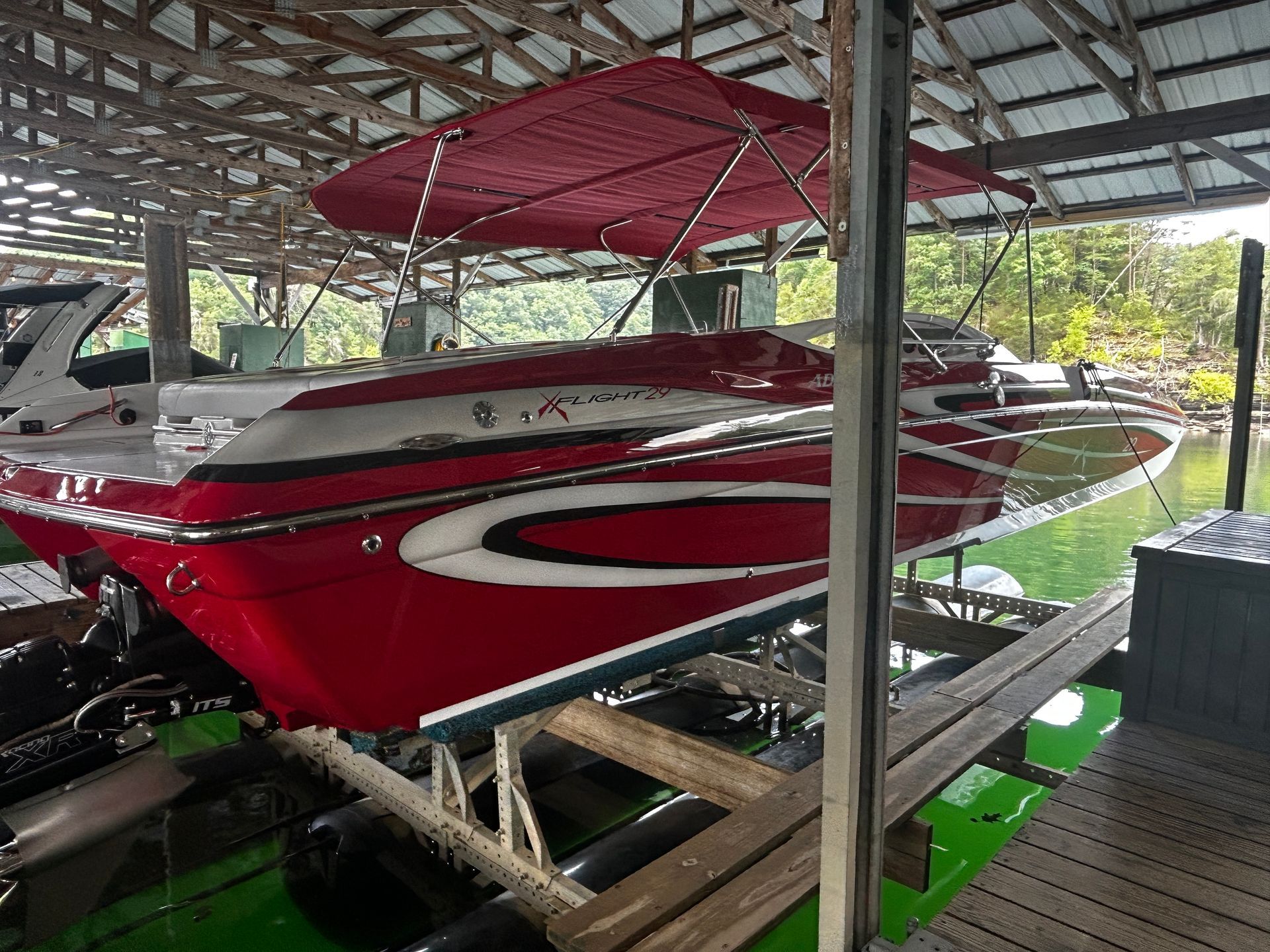 Red speedboat with white stripes stored on a trailer under a covered dock