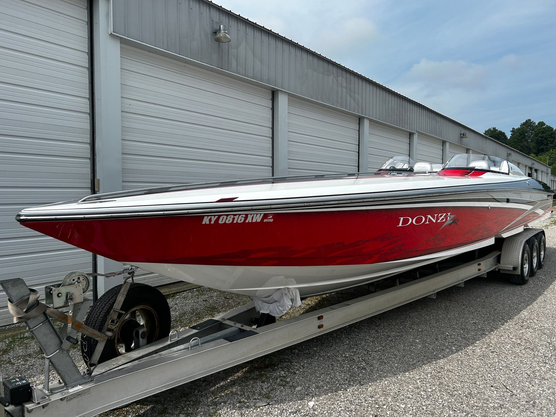 Red and white speedboat on a trailer beside a warehouse.