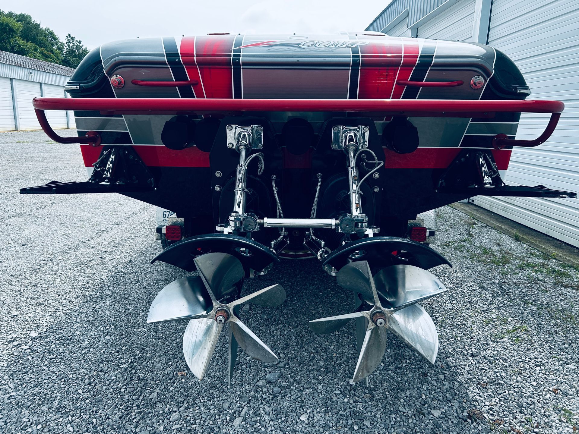 Rear view of a red racing boat with twin propellers and exposed engines on a trailer