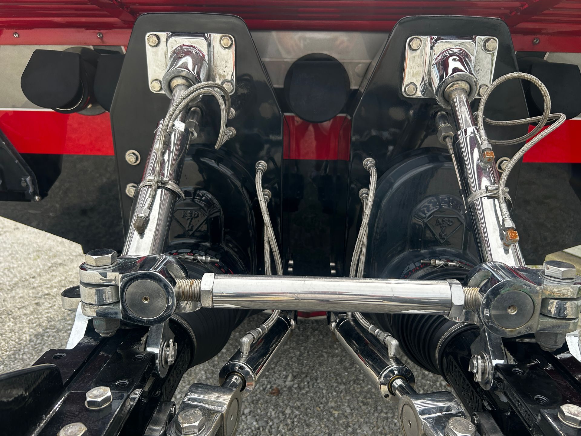 Close-up of two black motorcycle footboards with chrome linkage and a silver crossbar.