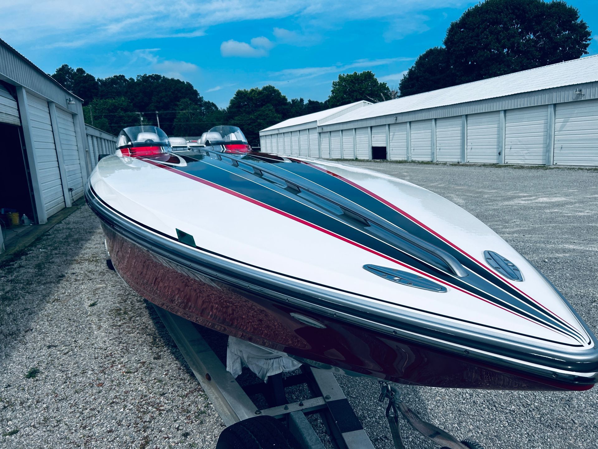 White and red speedboat on a trailer in a gravel lot, with storage units in the background