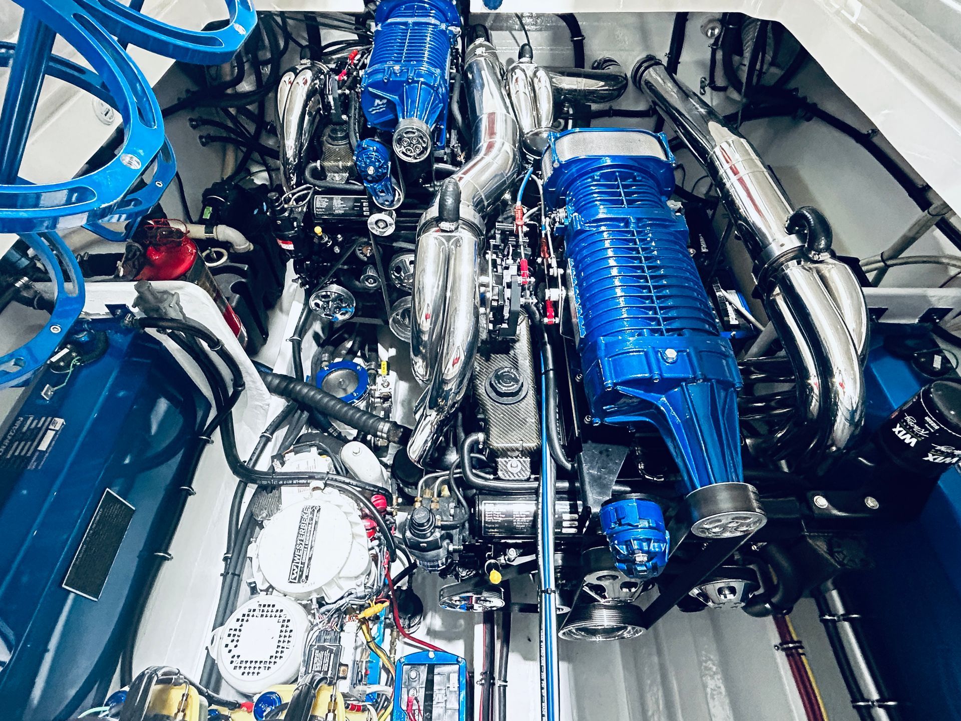 Blue car engine bay with polished chrome pipes and visible turbo components
