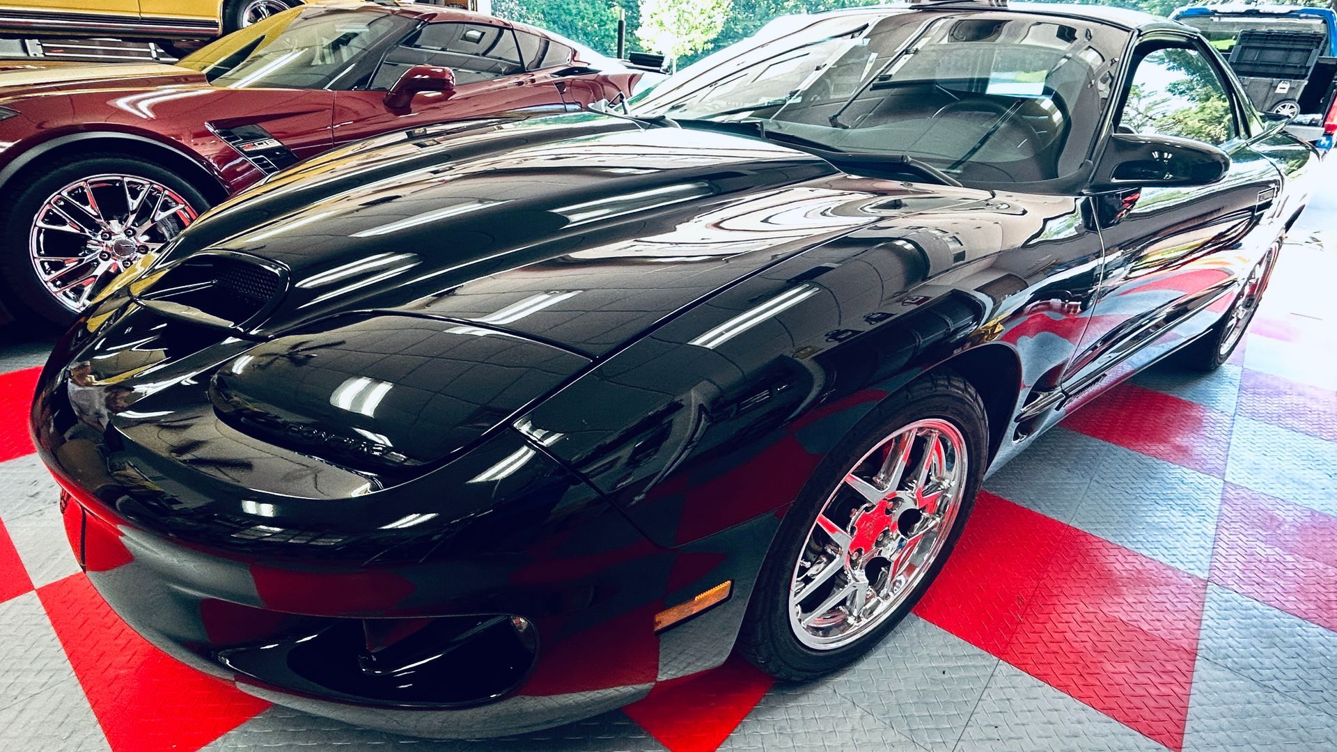Black sports car on a red-and-black checkered showroom floor, with a red car behind it
