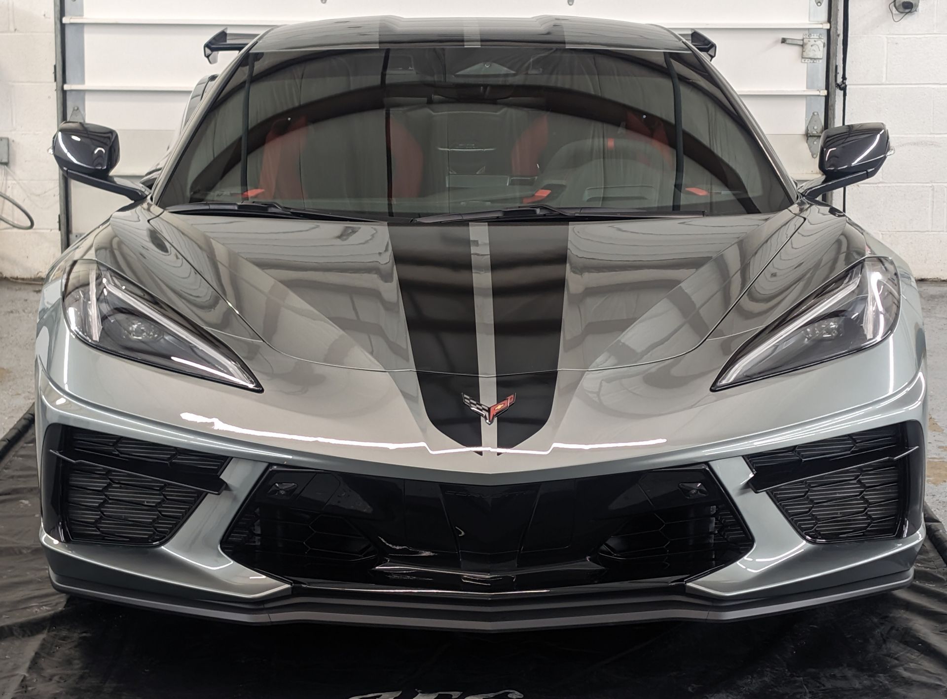 Front view of a silver sports car with black racing stripes parked indoors.