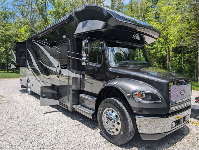 Black and silver motorhome parked on gravel beside trees, with awning extended