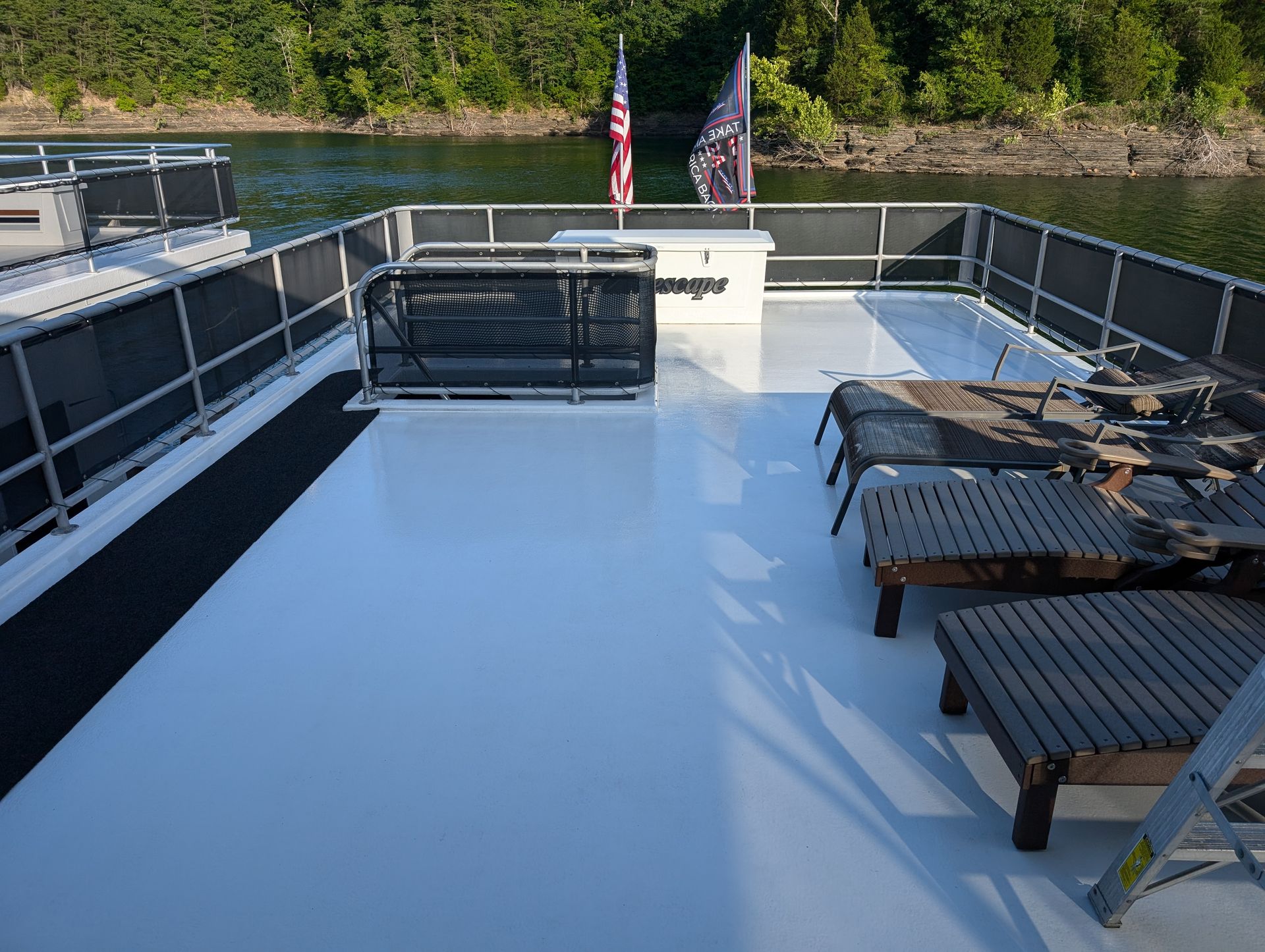 Boat deck with glossy white floor, railings, lounge chairs, and American flags by the water
