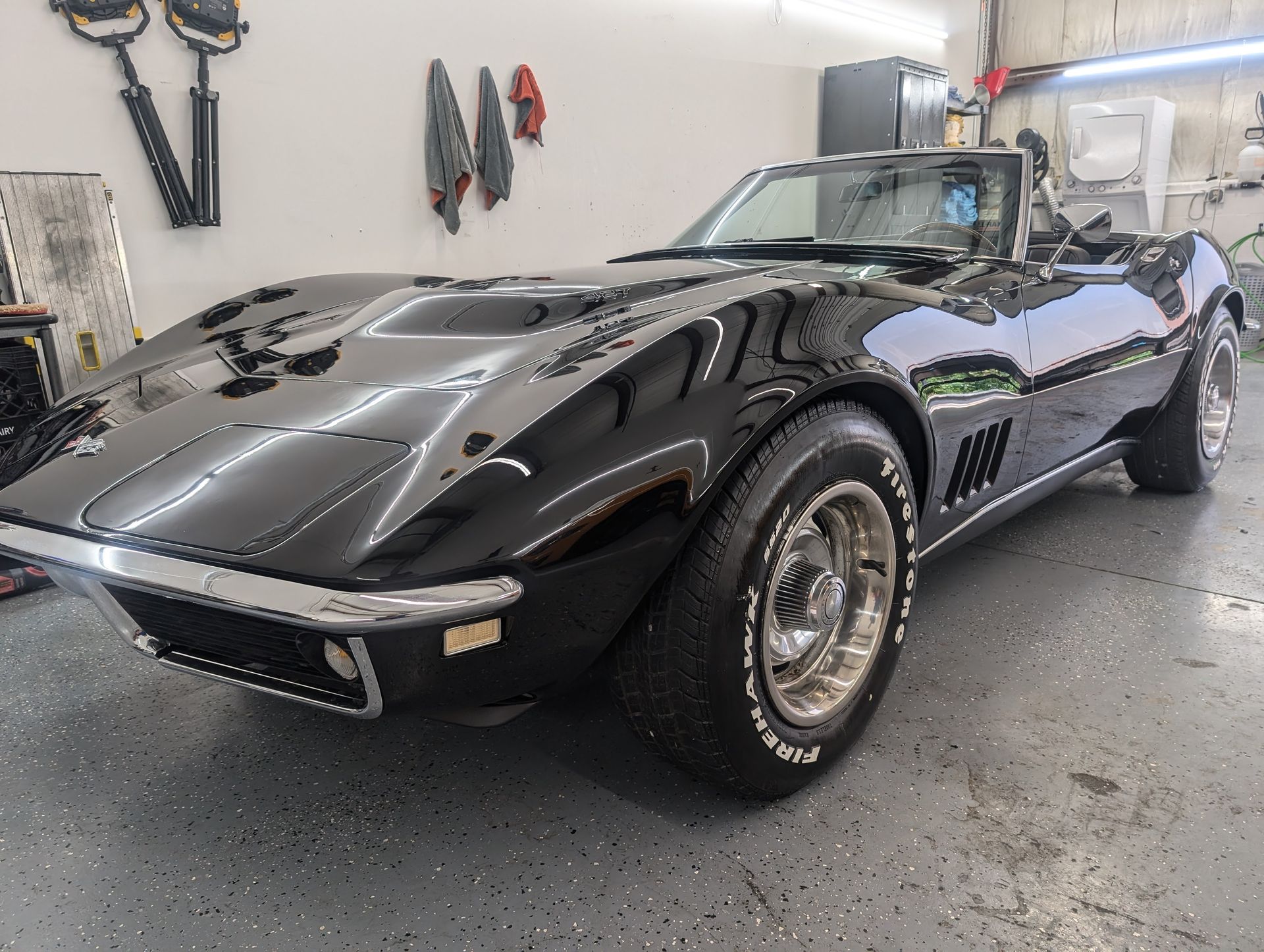 Black classic sports car in a workshop, shown from the front-left side.