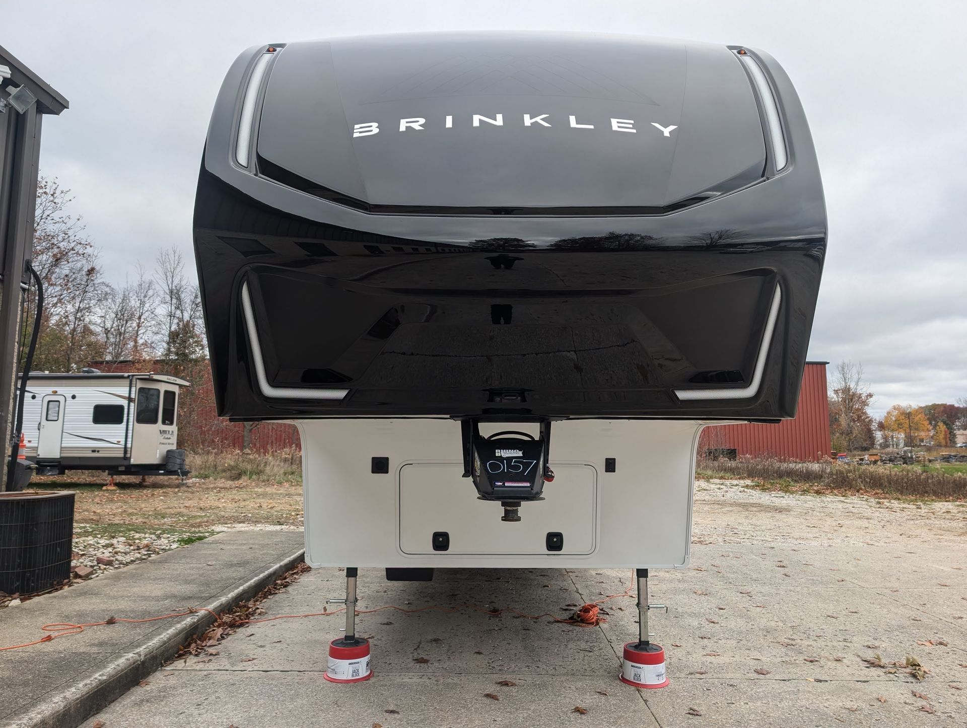 Front view of a black-and-white Shinkoey travel trailer parked on gravel with stabilizer jacks down
