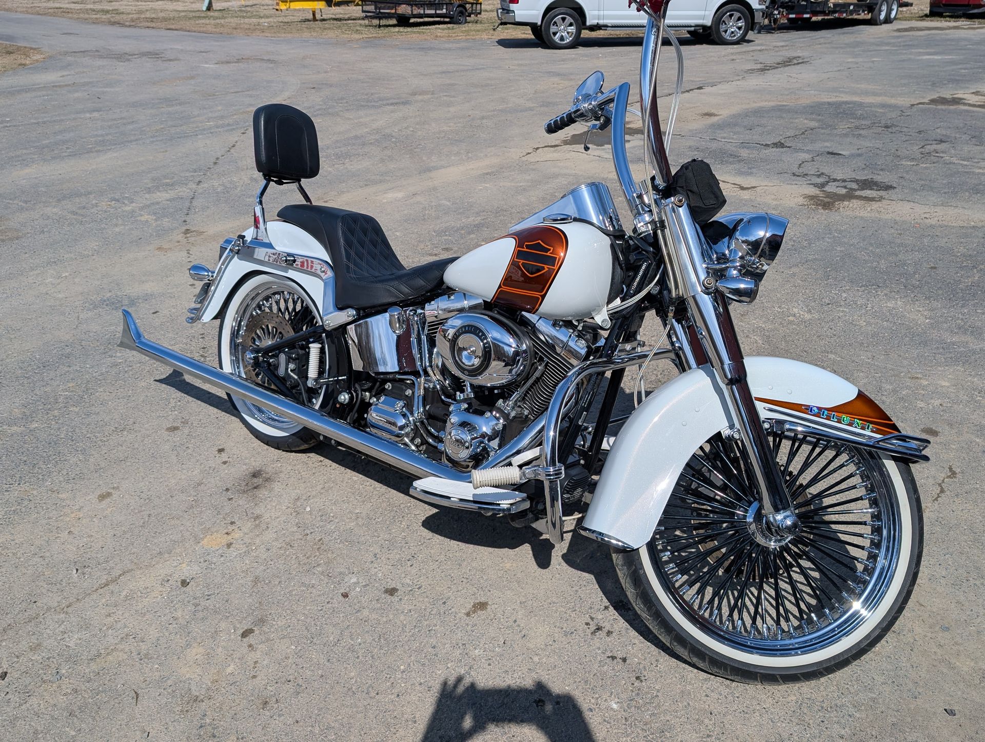 Custom white and orange motorcycle parked on a gravel lot, with chrome details and tall handlebars
