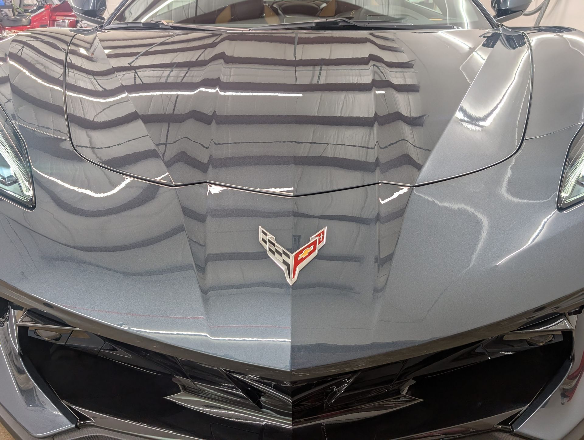Front view of a gray Chevrolet Corvette hood and emblem reflecting overhead lights.
