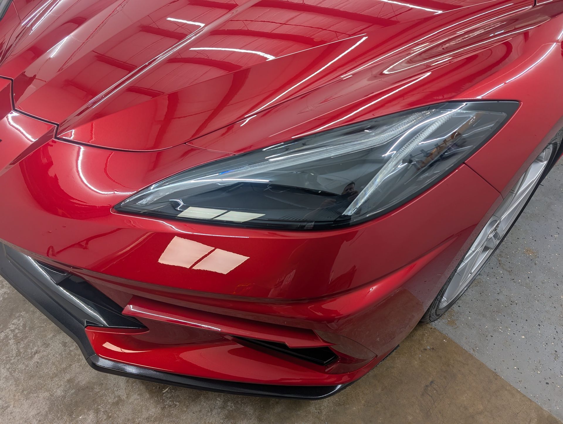 Close-up of a red sports car’s front headlight and bumper in a garage