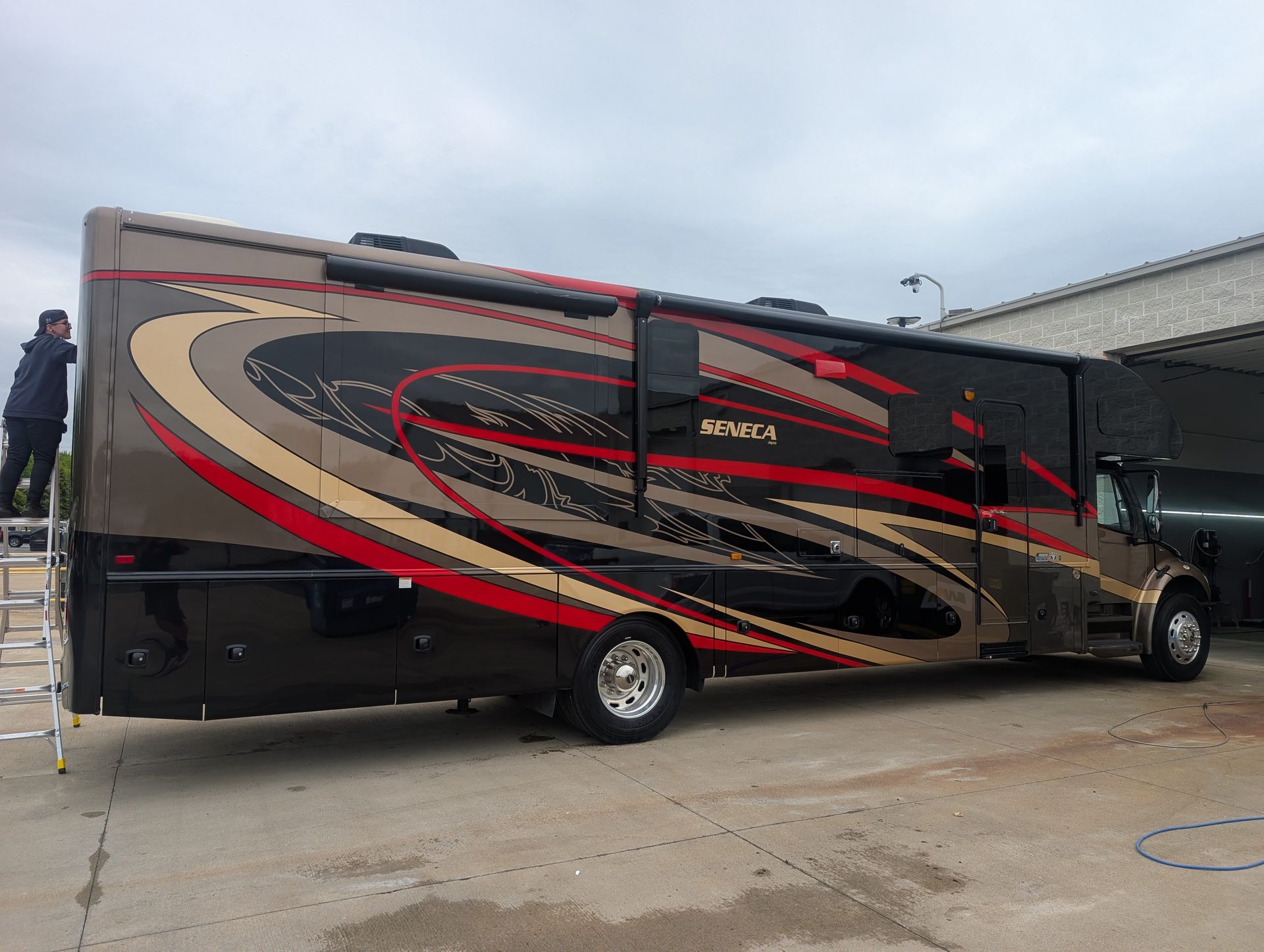 Black and tan RV bus with red swirl graphics parked beside a building on a concrete lot