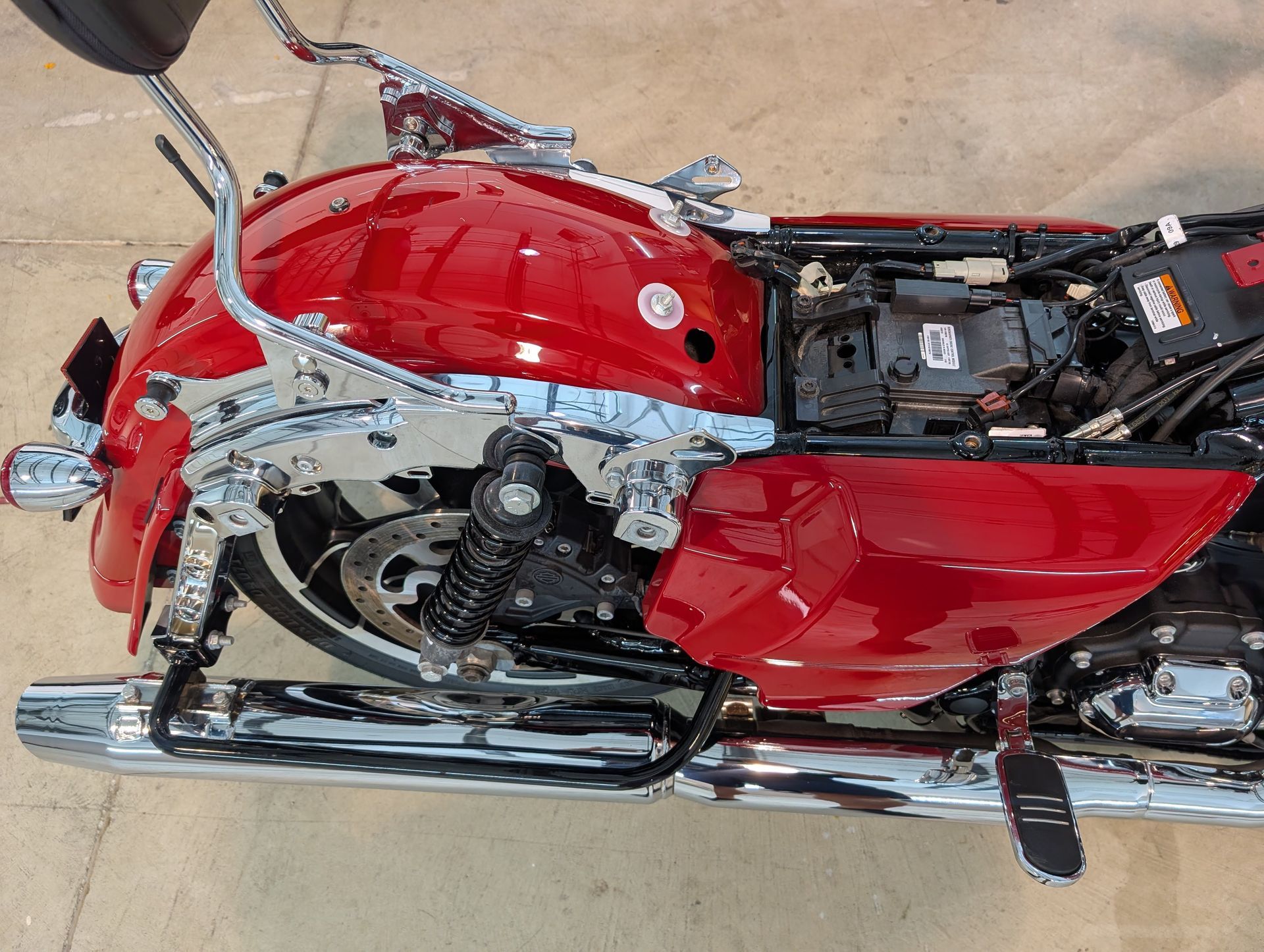 Red motorcycle with chrome engine and black seat, viewed from above on a sandy surface.