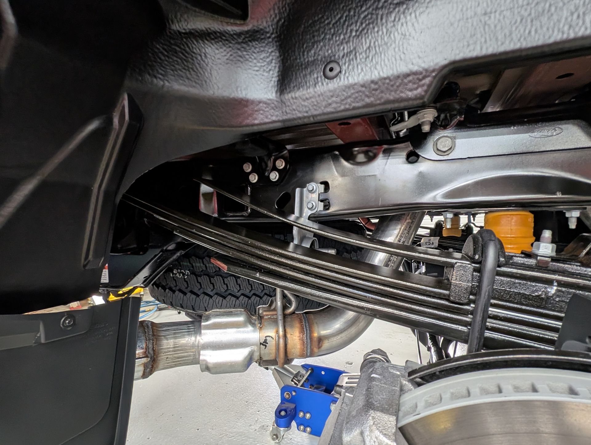 Vehicle undercarriage with exposed suspension components, wiring, and a blue bracket near the wheel area