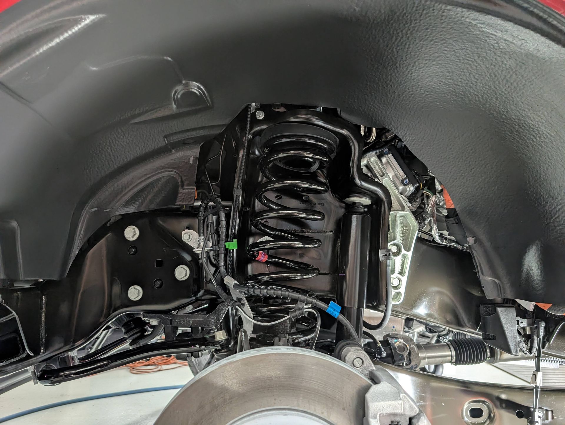 Car wheel well showing suspension strut, spring, brake assembly, and black inner fender liner