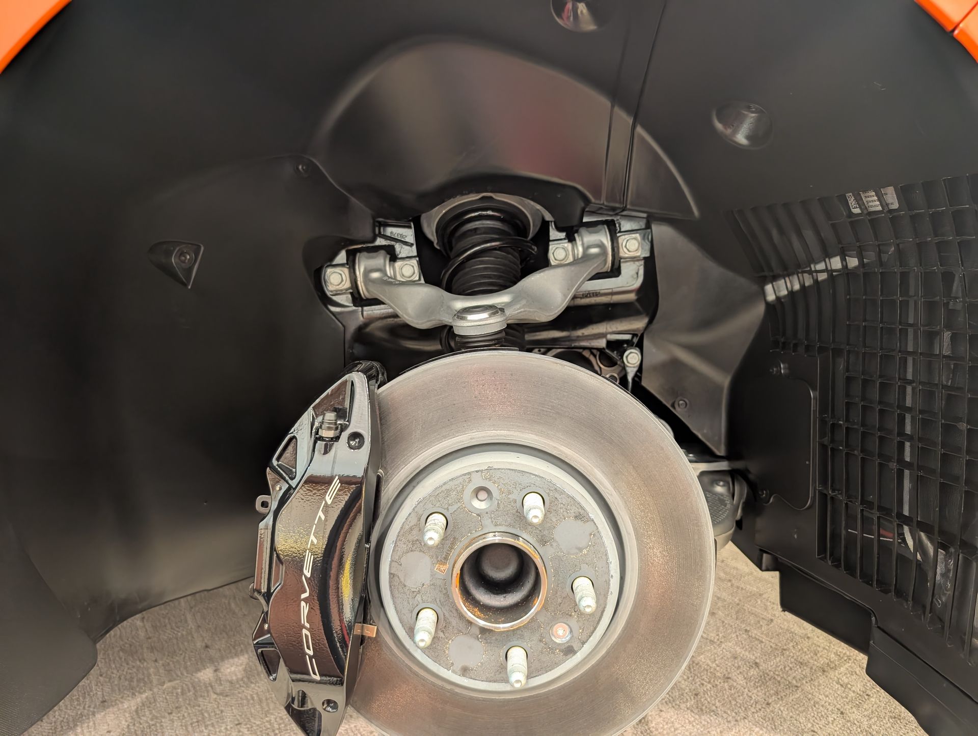 Close-up of a car wheel and brake assembly inside the wheel well, showing the suspension and rotor.