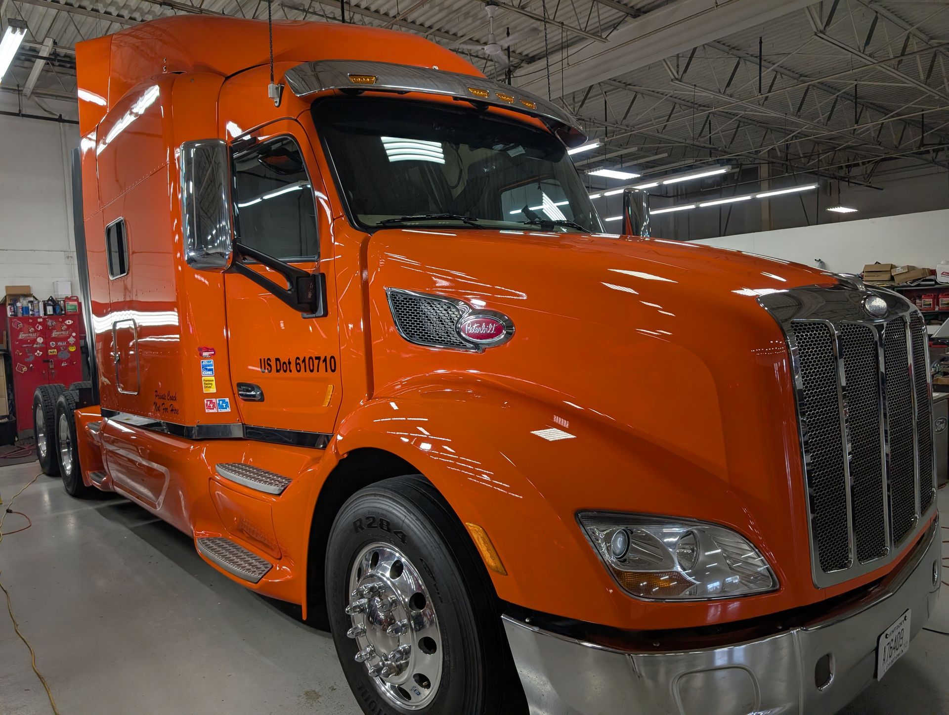 Orange semi-truck parked indoors at a warehouse, front-left view.